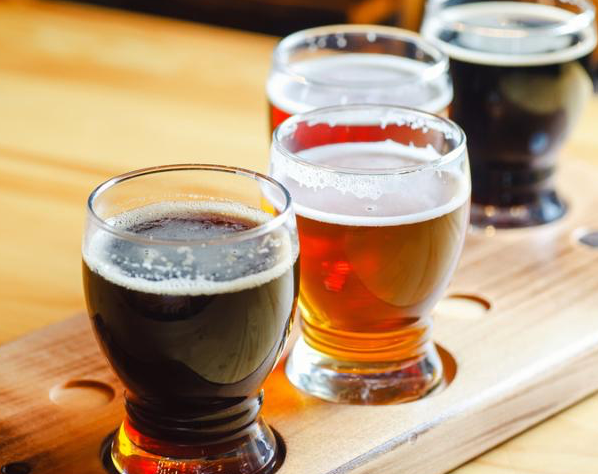 Flight with various types of craft beer in small glasses on a wooden table in a pub